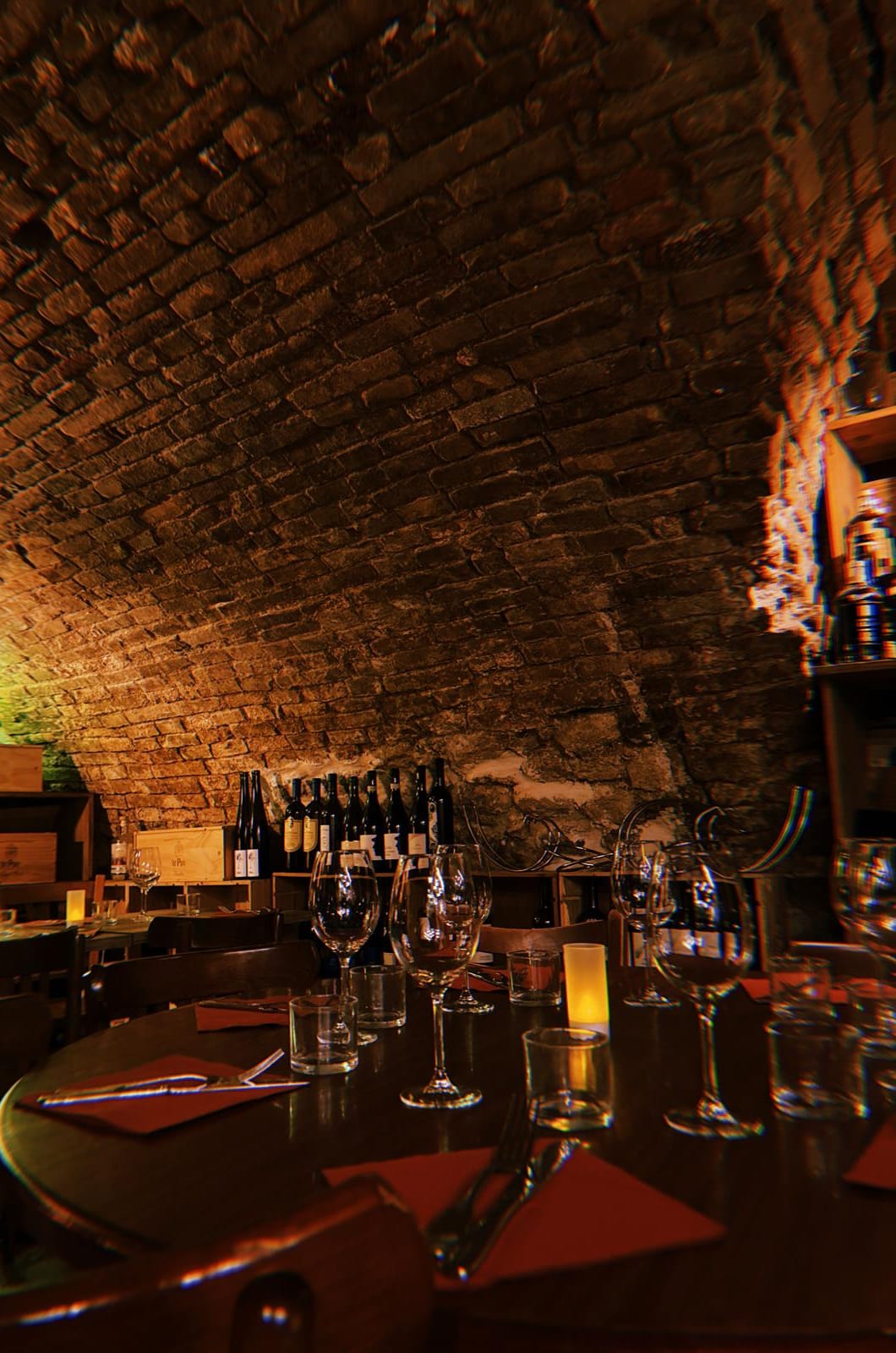 Voûte de pierre de la cave, table dressée et bouteilles de vin nature en fond