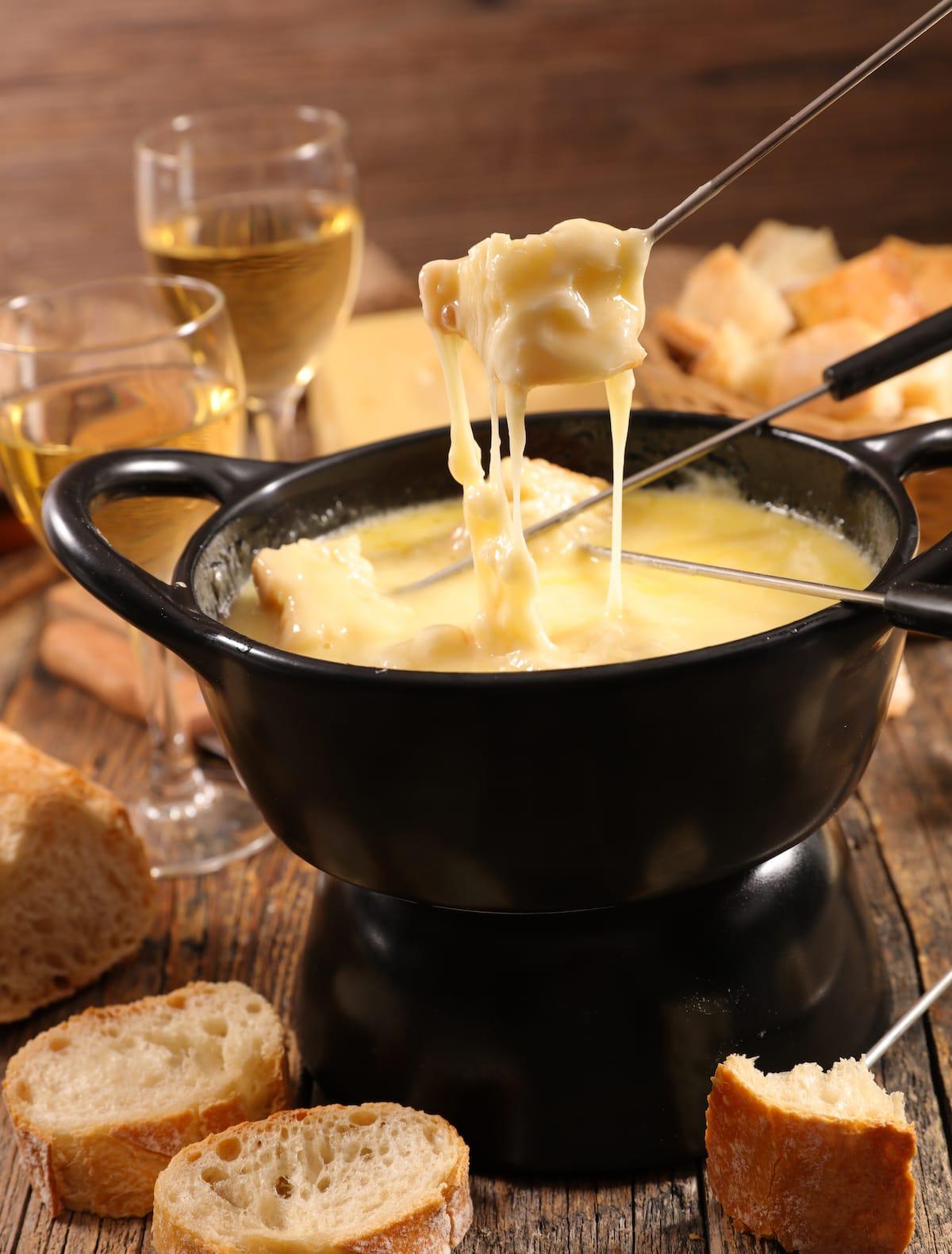 Fondue au fromage filante remontée à la fourchette au-dessus du caquelon, pain et vin blanc
