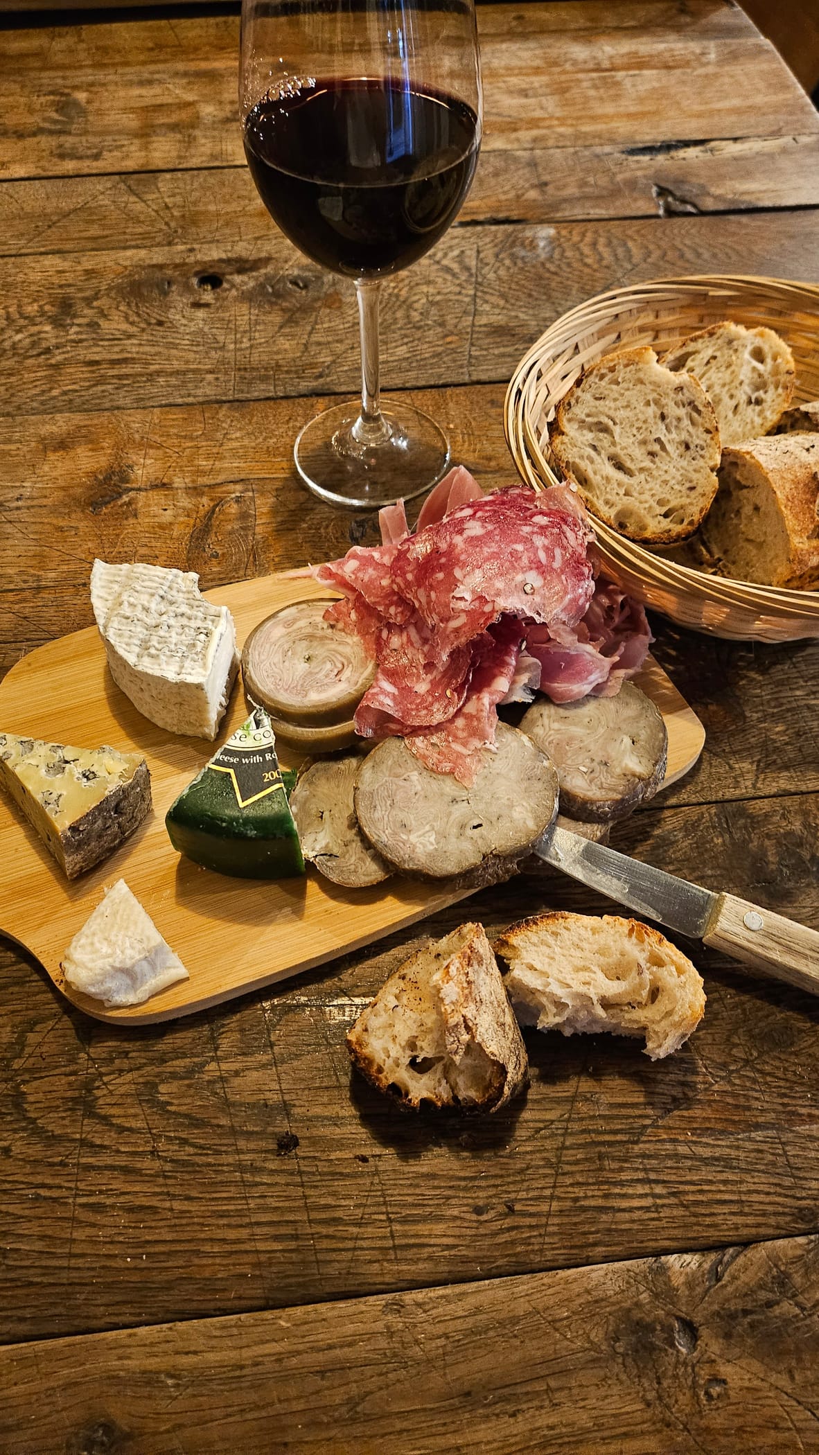 Planche de fromages affinés et de charcuterie, verre de vin rouge, sur une table en bois de la cave