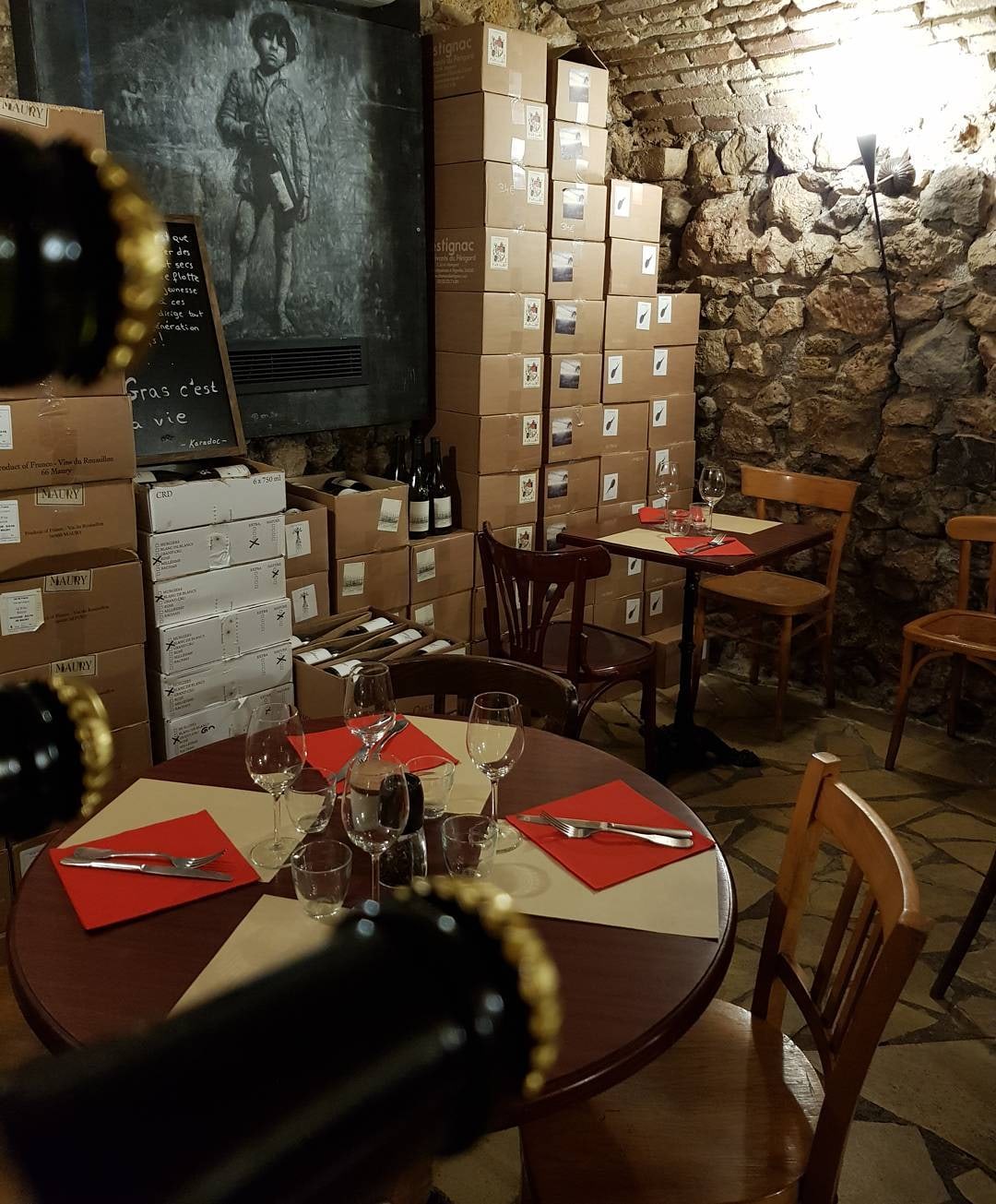 Salle de la cave, caisses de vin le long du mur de pierre et table ronde dressée
