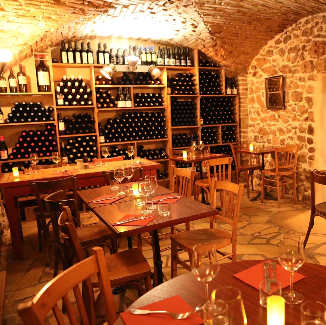 Salle voûtée en pierre, étagères de bouteilles et tables dressées aux bougies