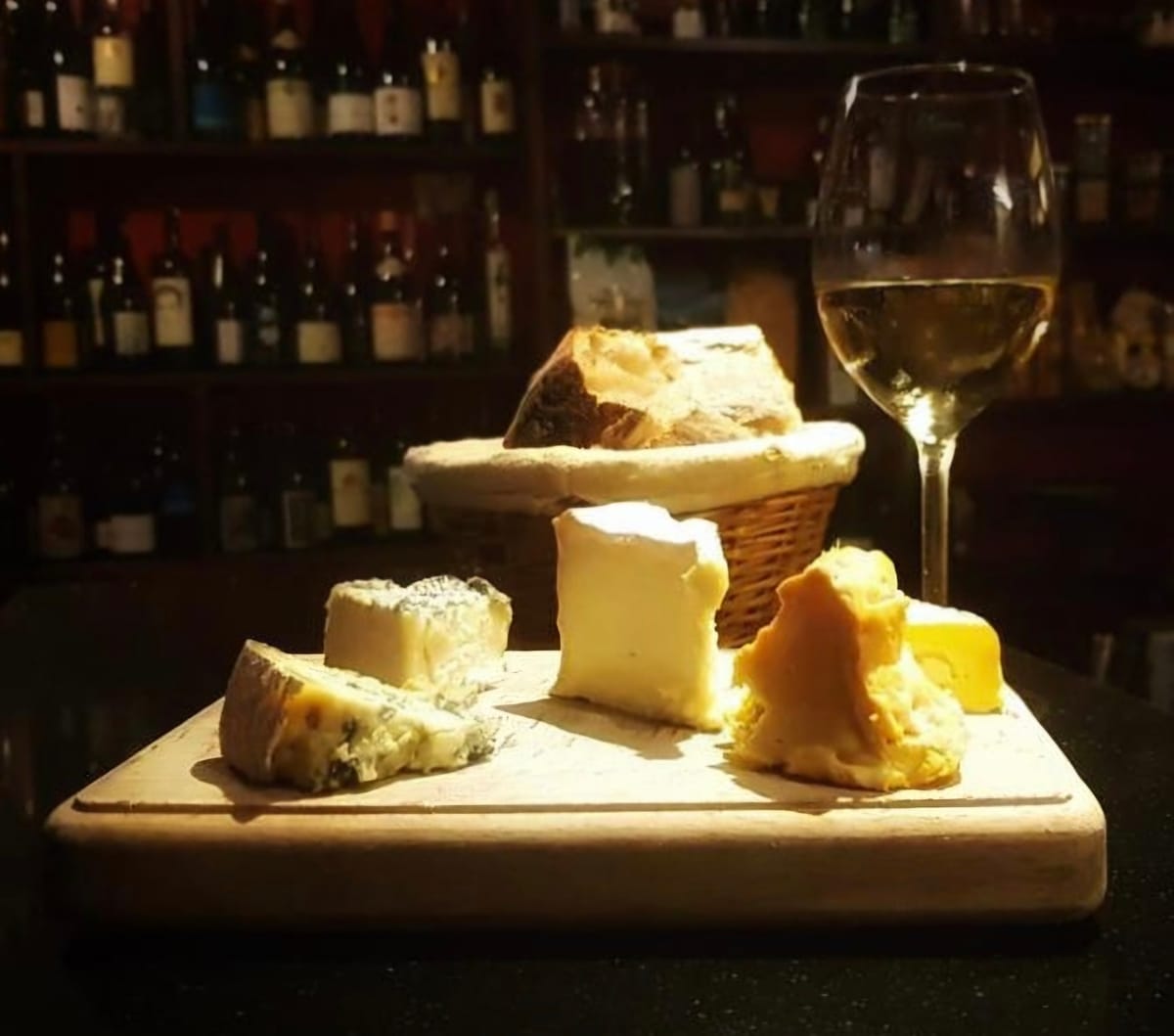 Sélection de fromages affinés servie avec du pain maison et un verre de vin blanc