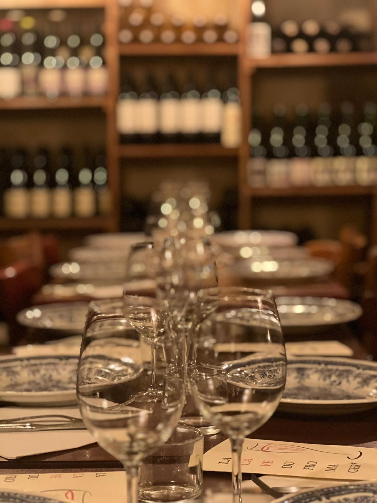 Grande tablée dressée, verres à vin alignés devant les rayonnages de la cave